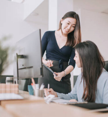 2 asian chinese white collar women having discussion in open plan office looking at files