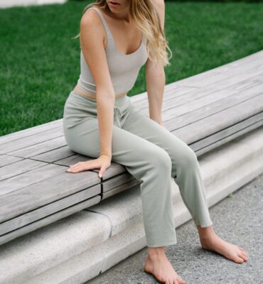 Woman sitting barefoot on a park bench wearing a casual loungewear outfit.